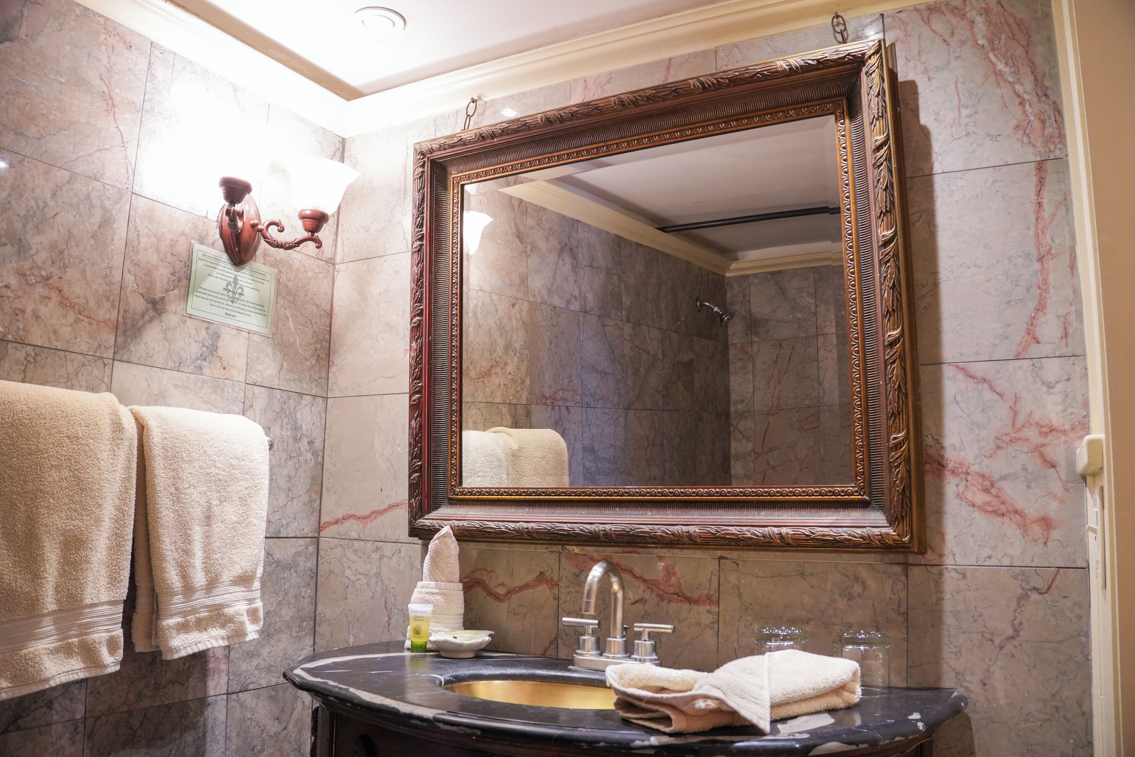 A bathroom with a marble wall, a large mirror, a sink, and towels.