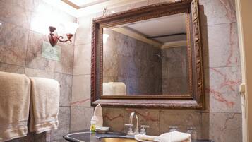 A bathroom with a marble wall, a large mirror, a sink, and towels.