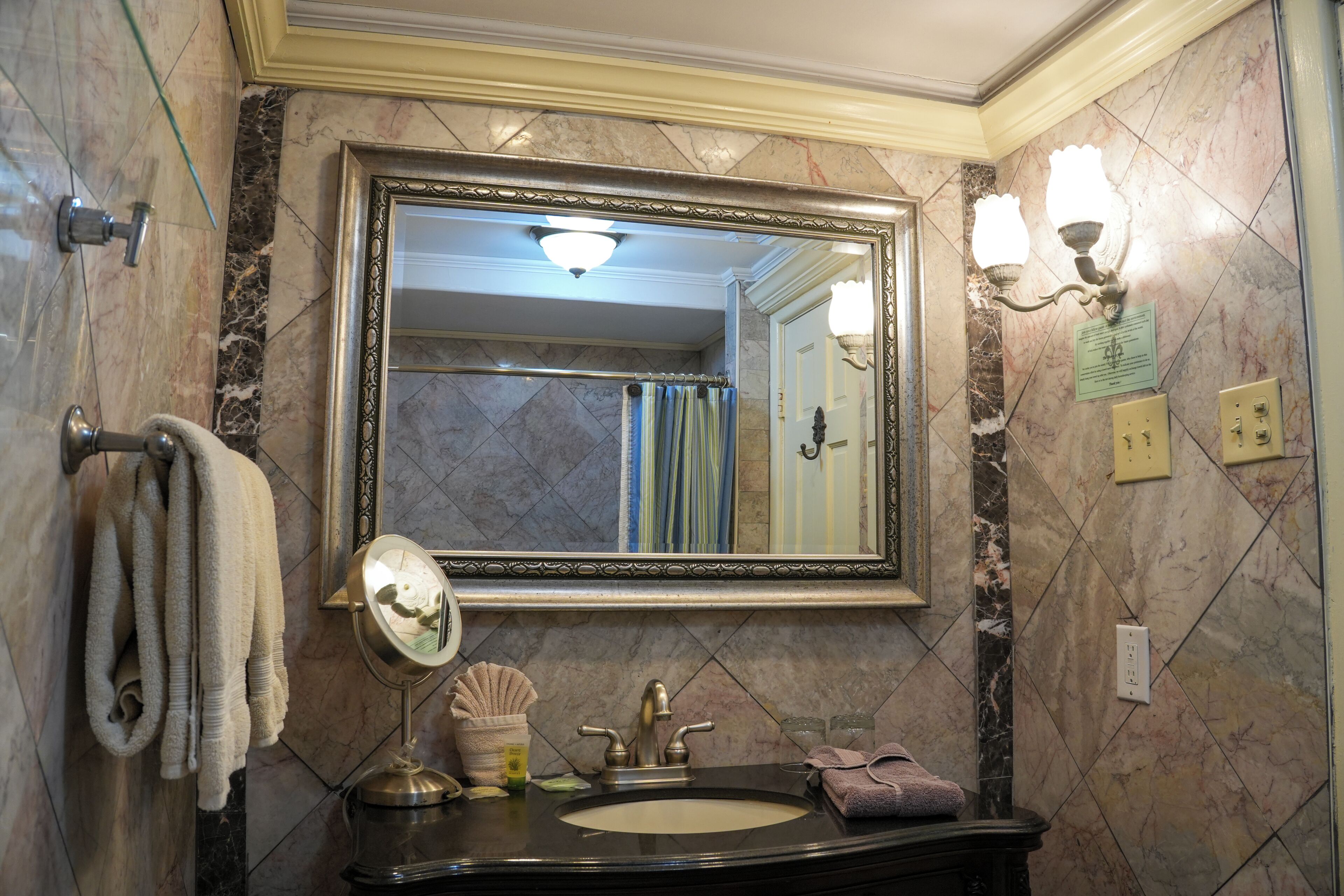 A bathroom with a large mirror, a sink, a towel rack, and a wall-mounted light fixture.
