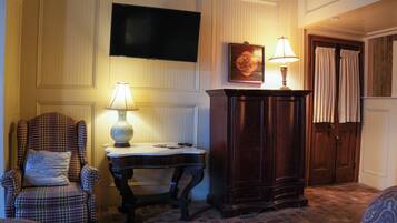 A room with a plaid armchair, a small table with a lamp, a wooden cabinet, and a television mounted on the wall.