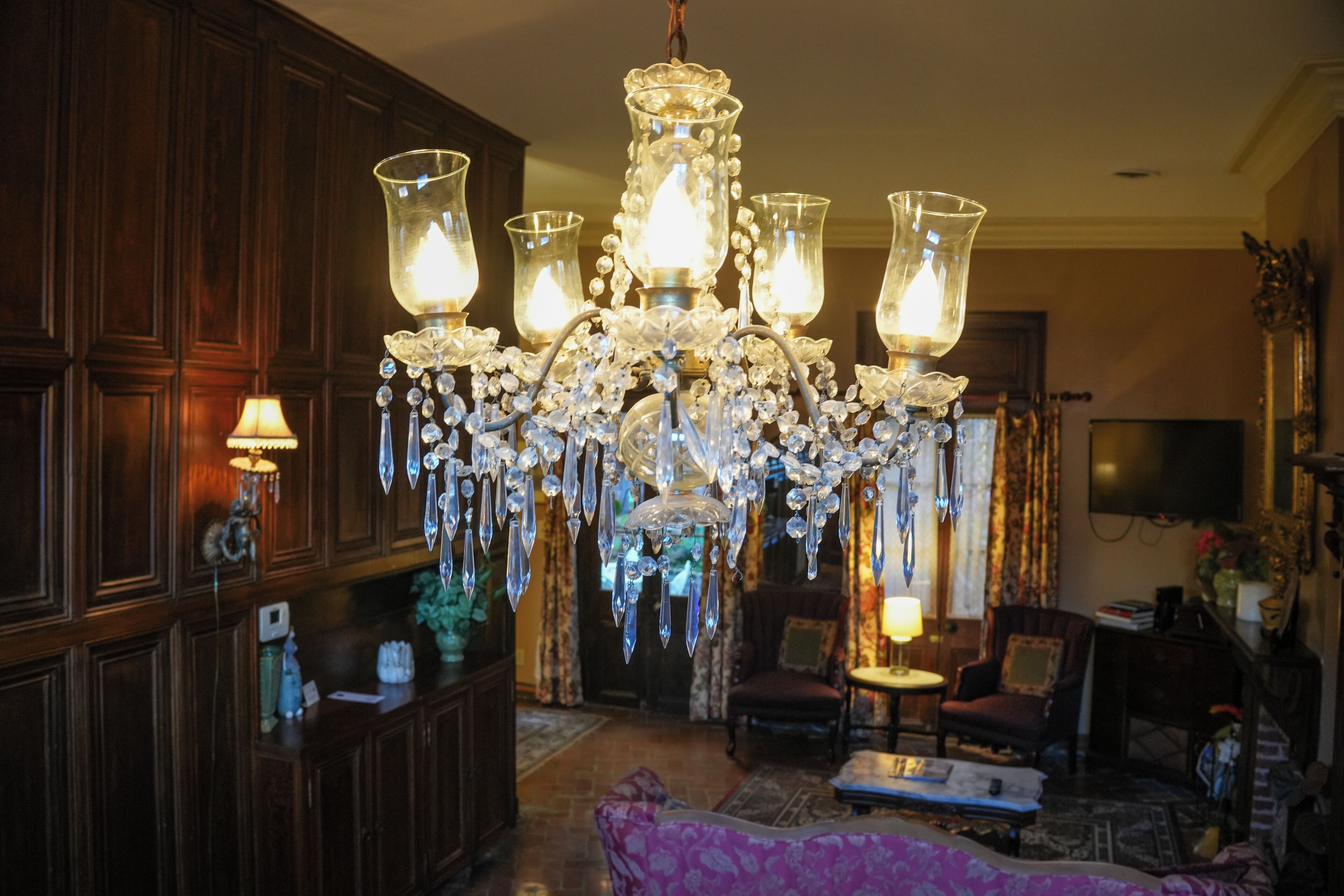 A chandelier with multiple glass shades, wooden paneling, a television, and a seating area with a patterned rug.
