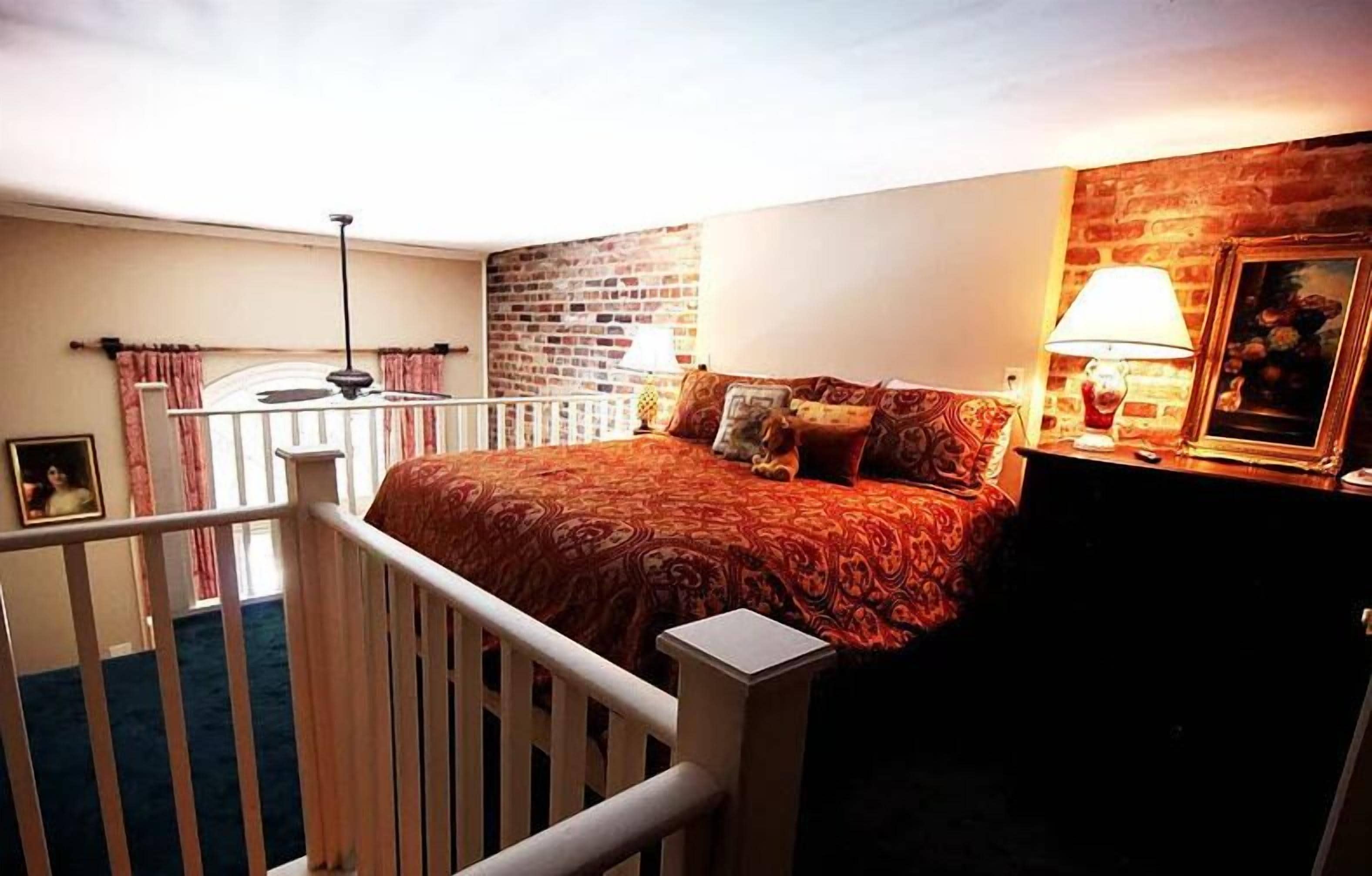 A bedroom with a bed, a nightstand, a lamp, a picture frame, and a brick wall.