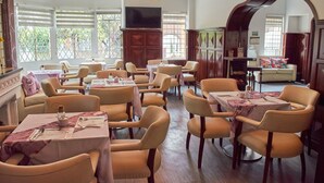 Un restaurante con varias mesas y sillas, un televisor montado en la pared y ventanas amplias con persianas.
