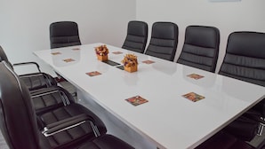 Un salón de conferencias con una larga mesa blanca, sillas de cuero negro y elementos decorativos sobre la mesa.