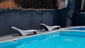 A swimming pool with tiled flooring and two white lounge chairs.