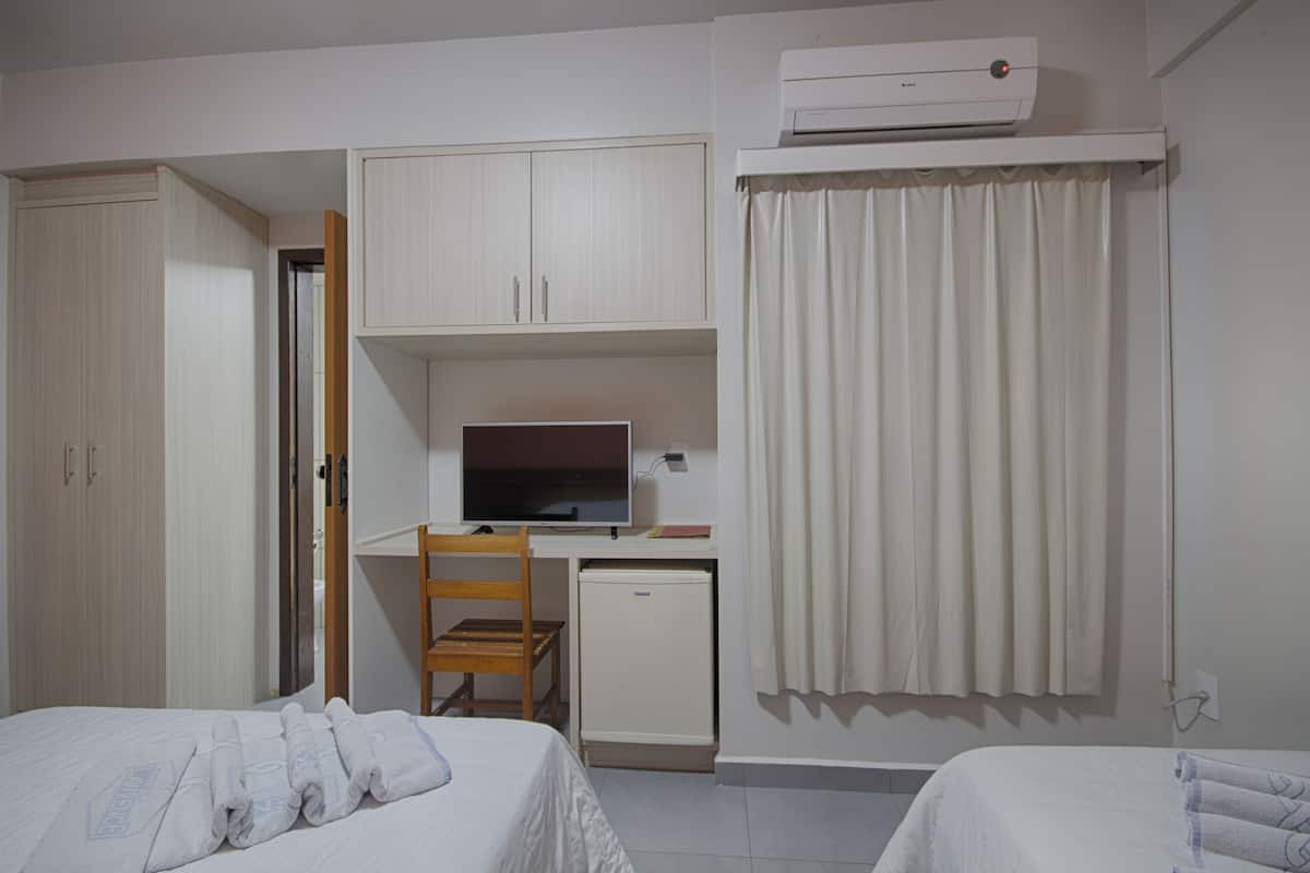Habitación de hotel con dos camas, un escritorio, televisión, refrigerador pequeño y aire acondicionado.