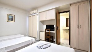 A hotel room with two single beds, a desk with a chair, a television, and a wardrobe. - Hotel Lawrence (Foz do Iguaçu)
