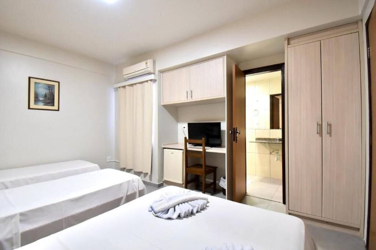 Una habitación de hotel con dos camas individuales, un escritorio con silla, un televisor y un armario.