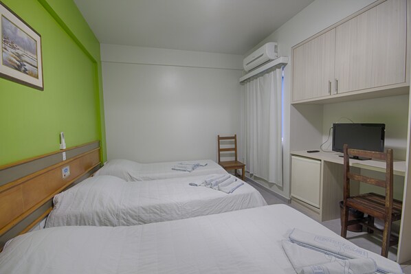 Una habitación de hotel con dos camas, un escritorio con computadora, una silla, un equipo de aire acondicionado y un cuadro en la pared.