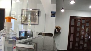 A reception area with a glass counter, a bottle of hand sanitizer, pendant lighting, a framed picture, and a wooden door with glass panels. - Hotel Lawrence (Foz do Iguaçu)