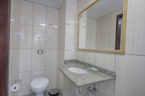 Une salle de bain avec des toilettes blanches, un lavabo doté d’un plan de travail en granit et un miroir avec un cadre en bois.
