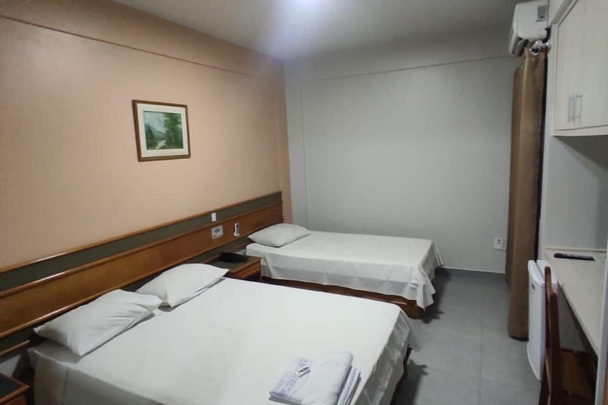 Una habitación de hotel pequeña con dos camas individuales, un cabecero de madera, una mesita y un cuadro en la pared.