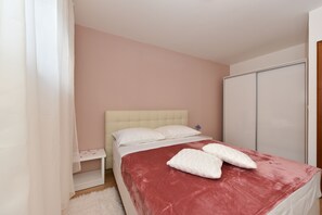 Quarto com cama, mesa de cabeceira, guarda-roupa e cortina branca.