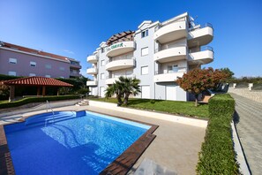 Um hotel moderno com piscina, várias varandas e um jardim bem cuidado.