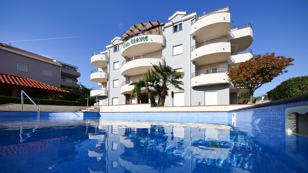 A multi-story hotel with balconies, a swimming pool, and palm trees. - Villa Gravić (Zadar)