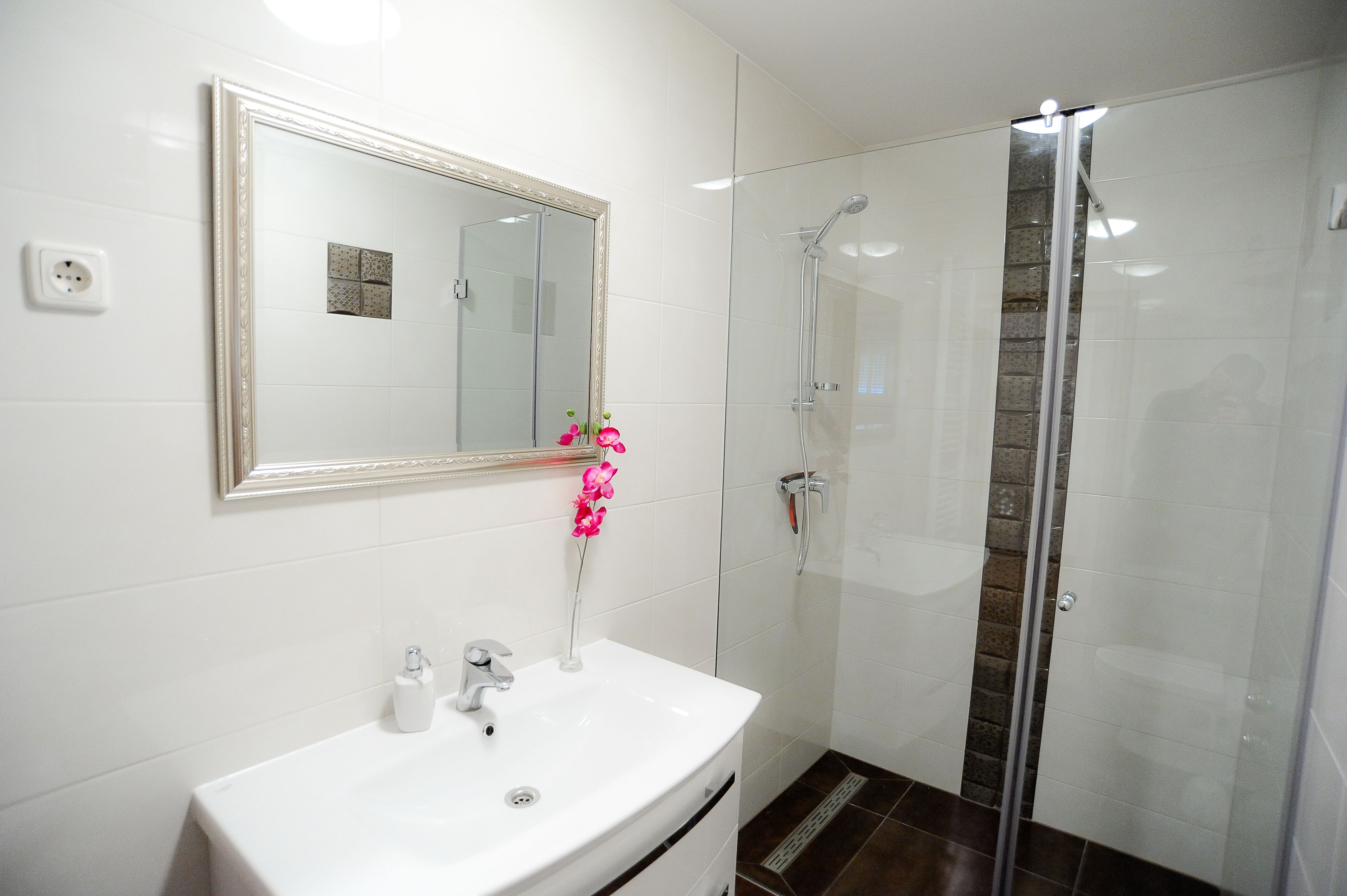 A bathroom with a white sink, mirror, and shower.