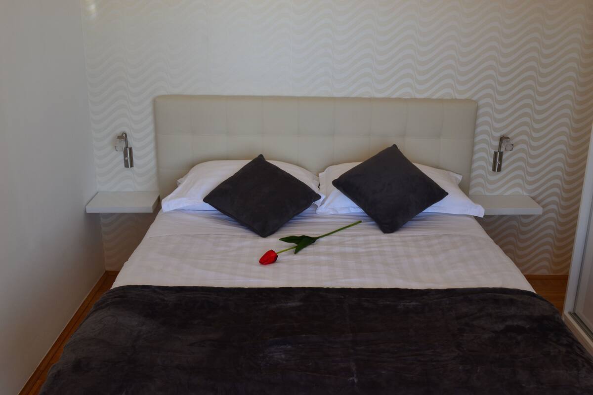 A neatly made bed with a white headboard, two black pillows, and a single red rose on the bed.