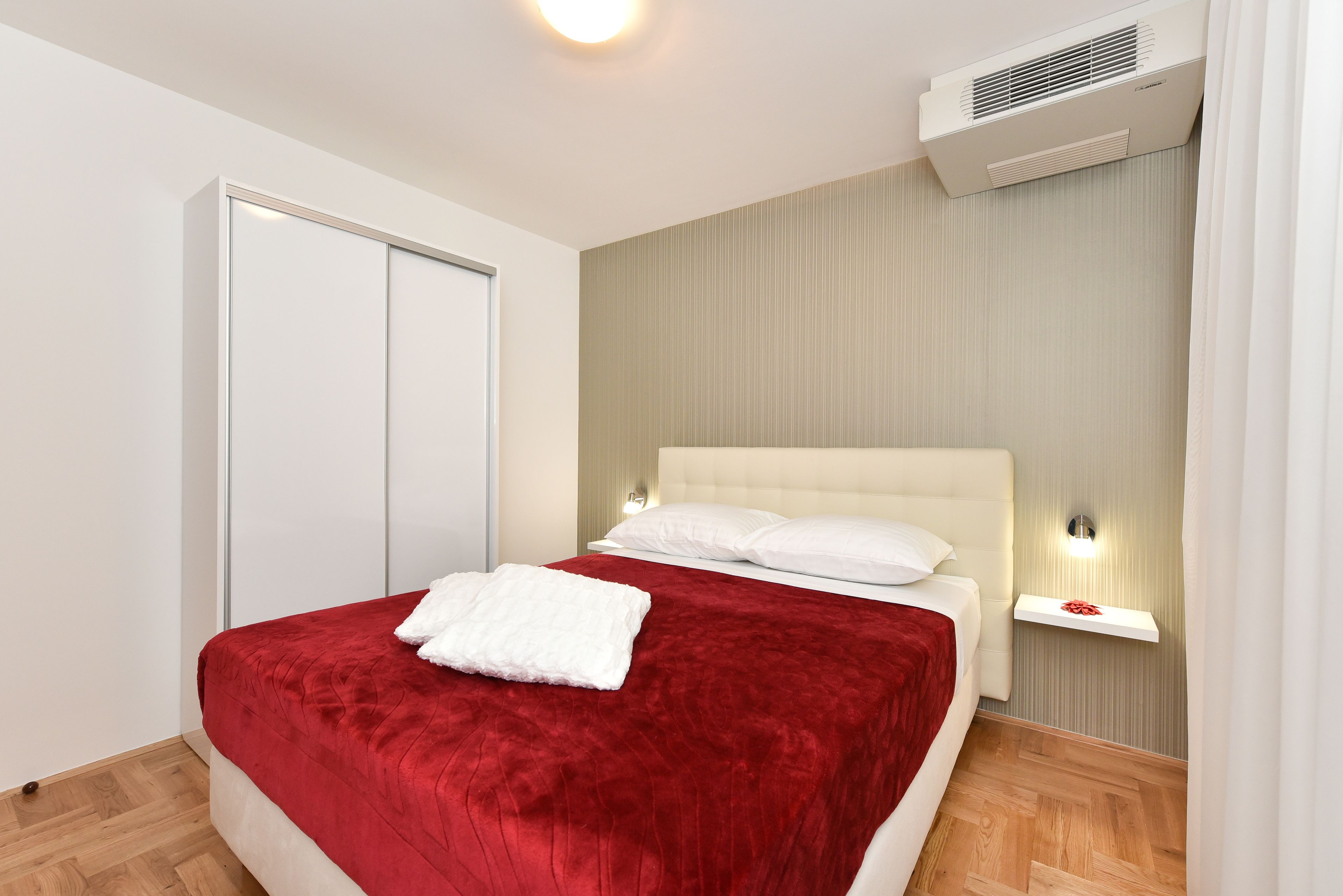 A neatly arranged bedroom with a bed, a bedside table, and an air conditioning unit on the wall.