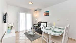 A modern living room with a dining area, featuring a sofa, a glass table, and a flat-screen TV on a white cabinet. - Villa Gravić (Zadar)