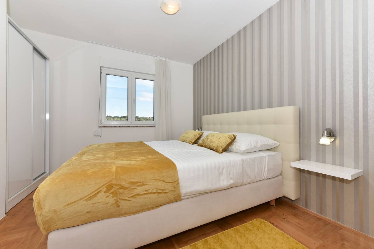 A bedroom with a bed, a window, a bedside table, and a wall-mounted light.