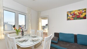 A dining area with a glass table, white chairs, and a view of the city through large windows. - Villa Gravić (Zadar)