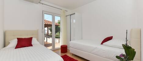 Una habitación de hotel moderna con dos camas, una alfombra roja, una planta en maceta y un ventanal corredero que da a un espacio exterior.