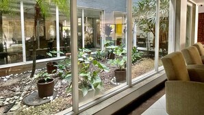 A modern interior with large windows, a seating area with chairs, and a variety of potted plants. - Ibiza Barra Hotel (Rio de Janeiro)