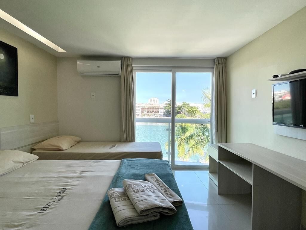 Une chambre d’hôtel avec un lit, un canapé, une télévision et un balcon offrant une vue sur les palmiers et les immeubles.