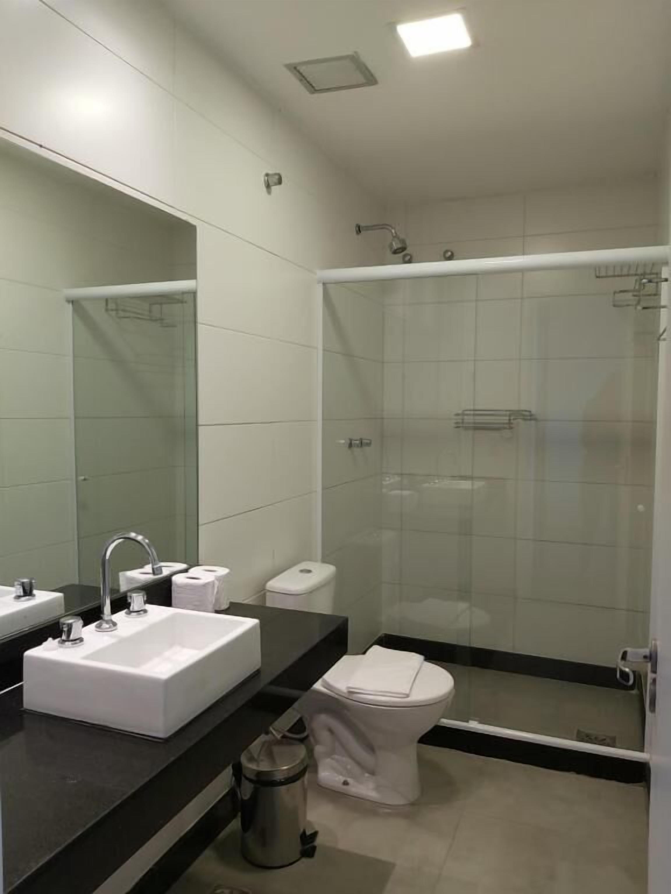 A modern bathroom with a large mirror, a sink, a toilet, and a glass-enclosed shower area.