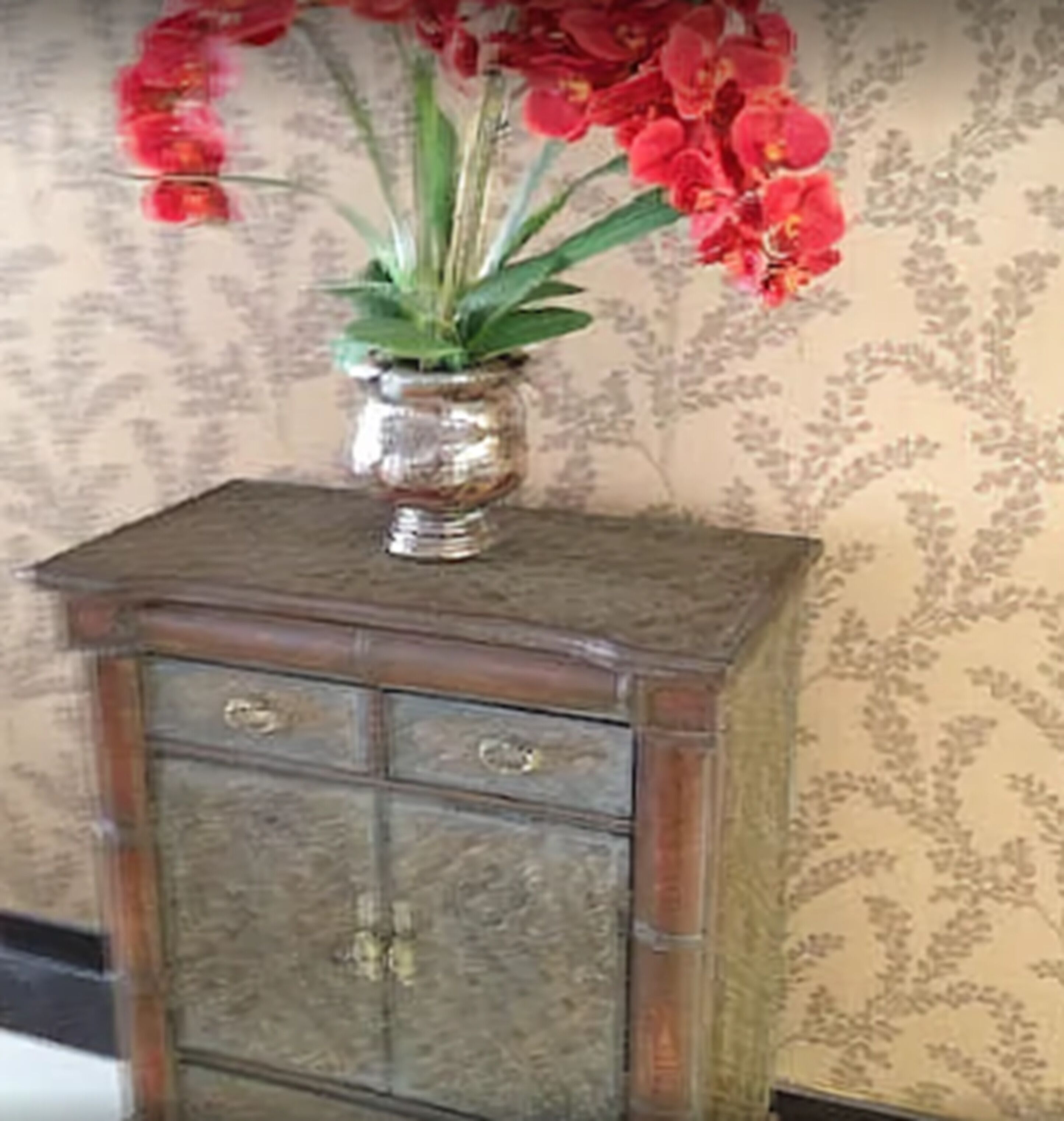 Un meuble en bois contenant un vase en verre rempli de fleurs rouges.