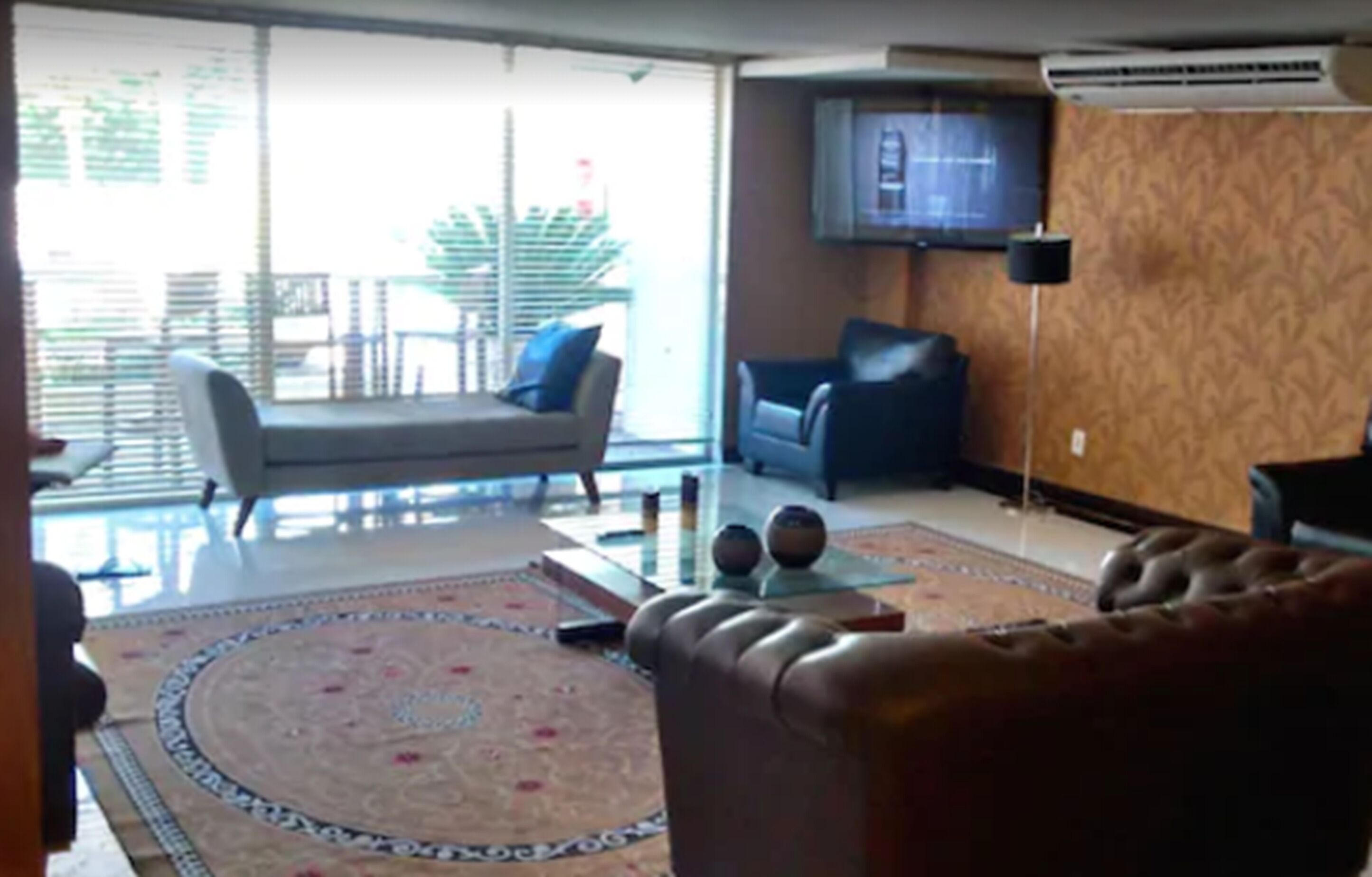 Un salón con sofá, una mesa de centro con objetos decorativos, un televisor montado en la pared y una alfombra estampada.