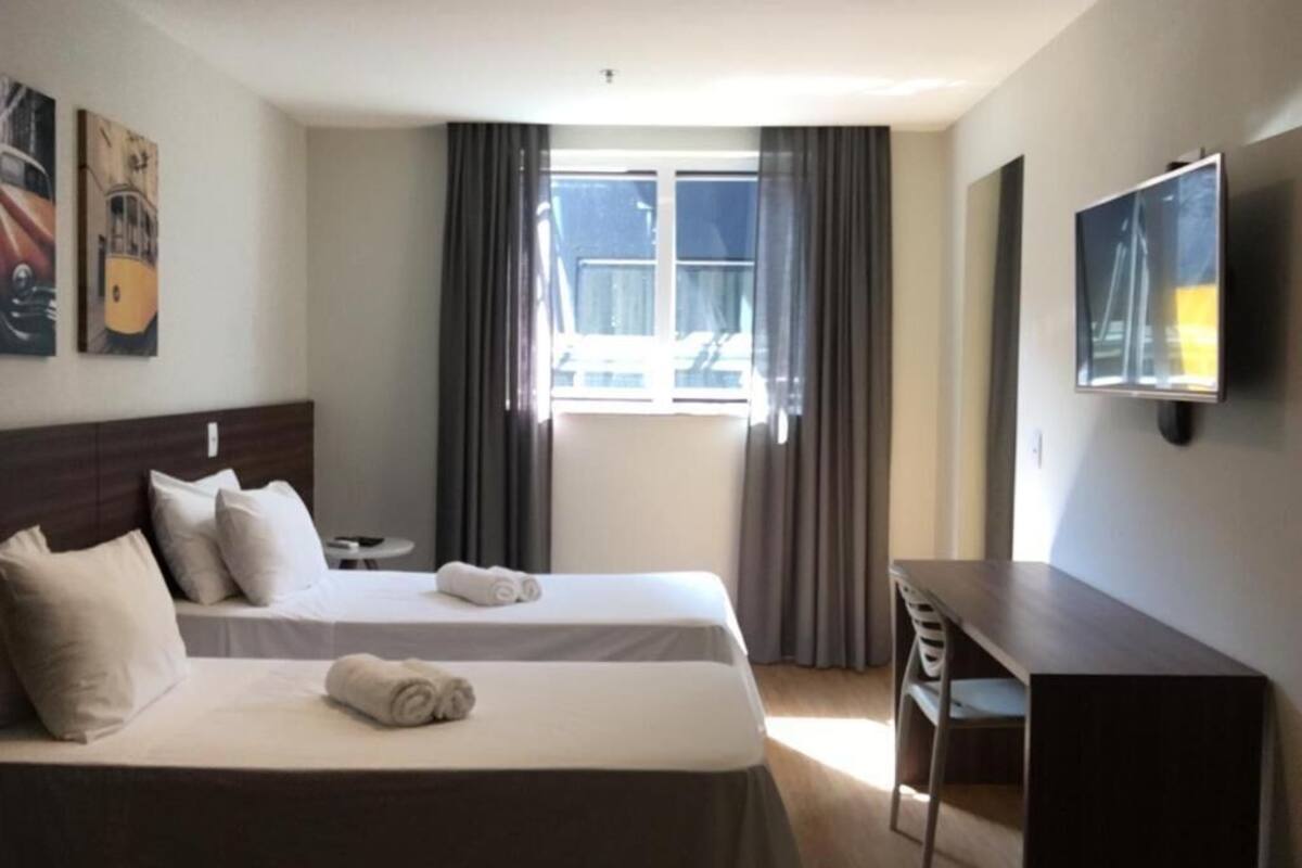 A hotel room with two beds, a desk, a chair, a TV, and a window with curtains.