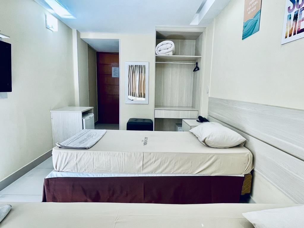 A compact hotel room with a bed, a small desk, a wardrobe, and a bathroom visible through an open door.