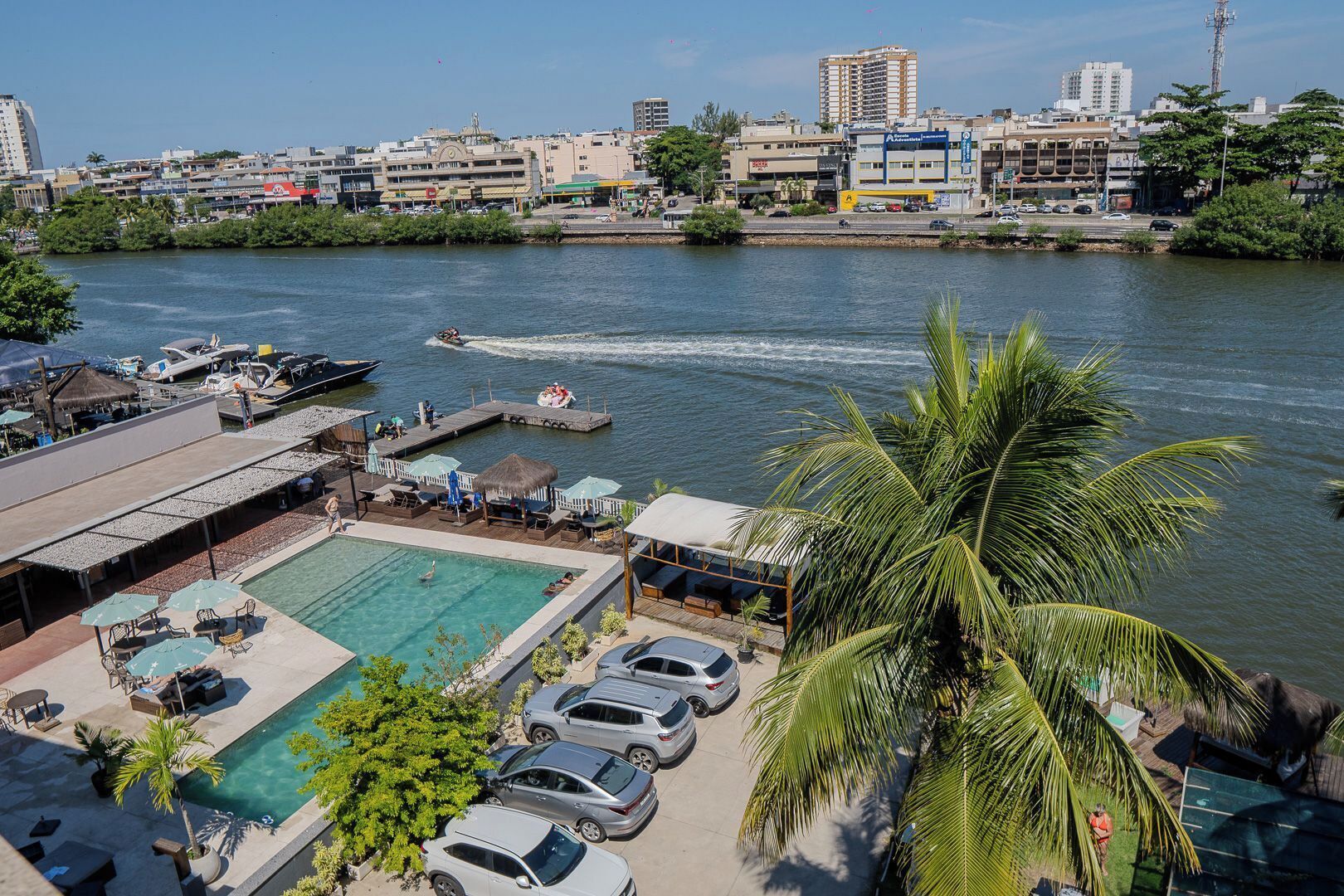 Un hôtel situé au bord de l’eau, doté d’une piscine, de bateaux amarrés et offrant une vue sur les gratte-ciel de la ville en arrière-plan.