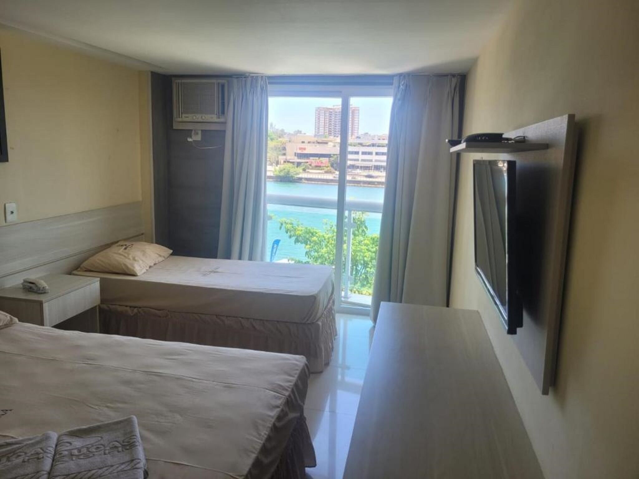 Ein Hotelzimmer mit zwei Betten, einem Fernseher und Blick auf ein Gewässer.
