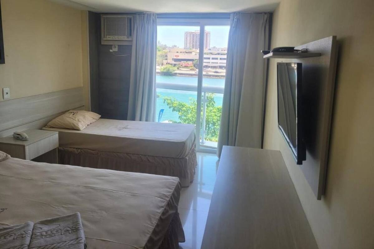 A hotel room with two beds, a TV, and a view of a body of water.