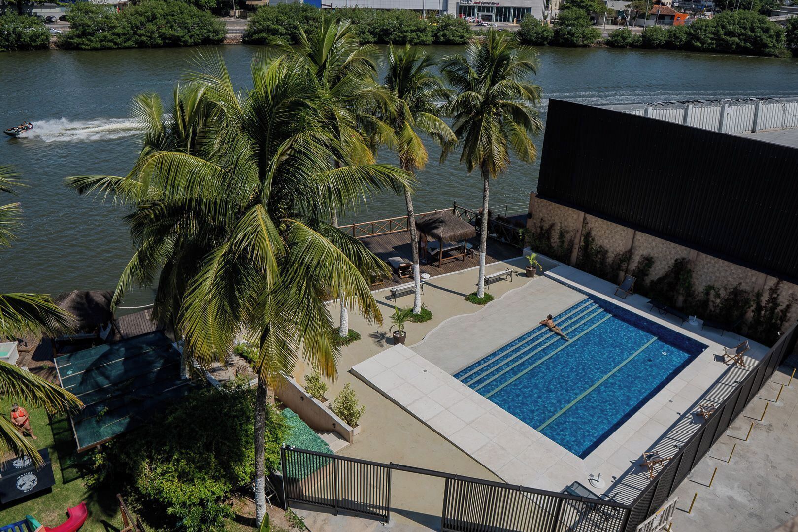 A swimming pool with a view of a river, surrounded by palm trees and a deck area with lounge chairs.