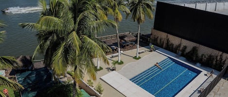 A swimming pool with a view of a river, surrounded by palm trees and a deck area with lounge chairs.