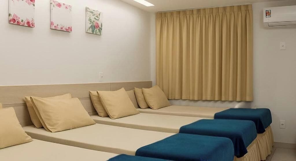 Una habitación con cuatro camas, ropa de cama color beige y un ventanal con cortinas color beige.