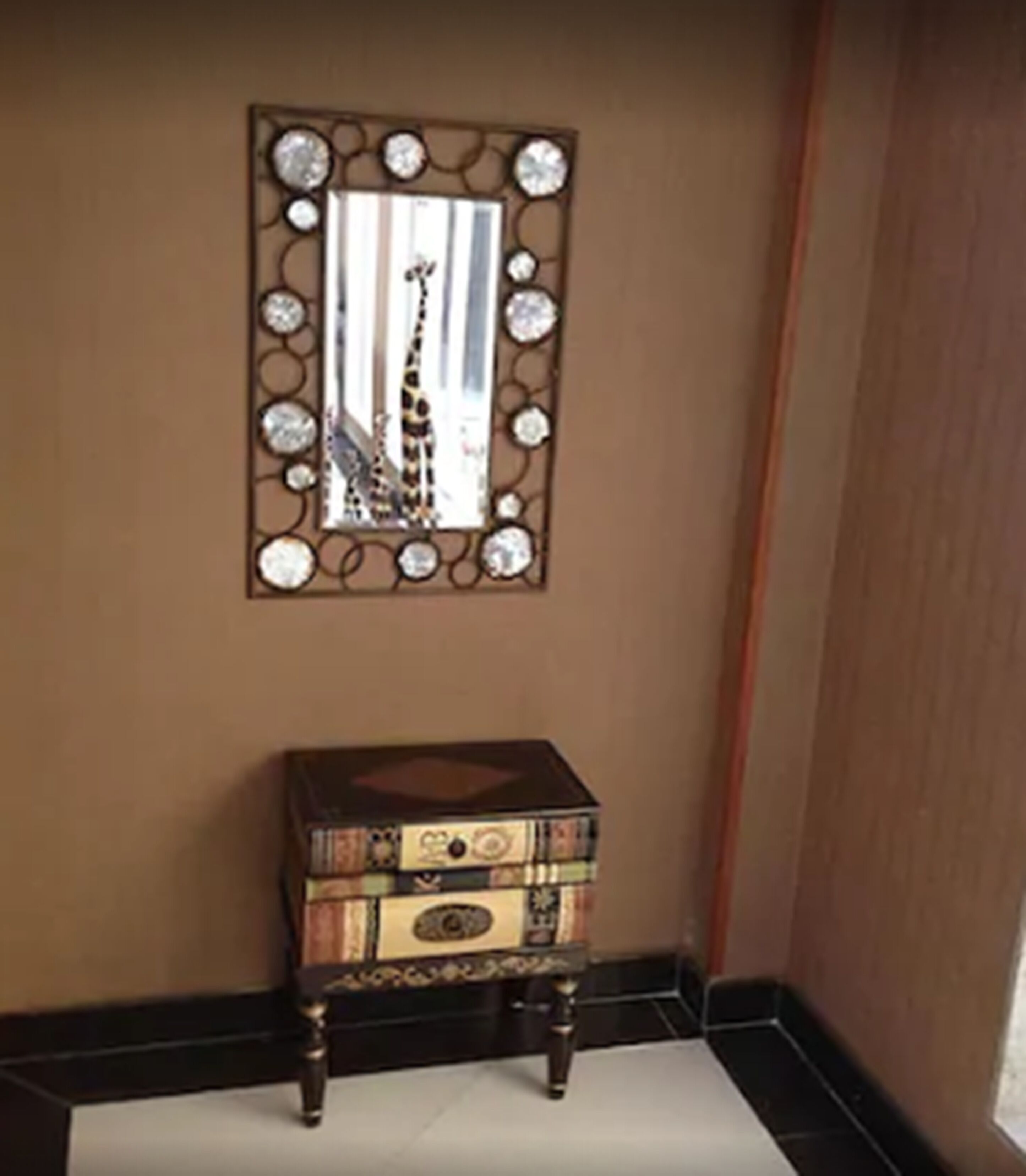 Una esquina con un espejo decorativo, un pequeño cofre de madera y una pared lisa.
