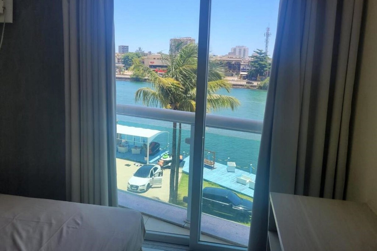 Een hotelkamer met een groot raam met uitzicht op een jachthaven met boten en palmbomen.