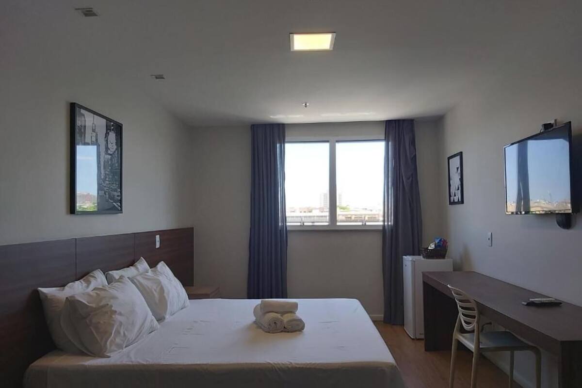 A hotel room with a bed, a desk, a chair, a TV, and a window with curtains.