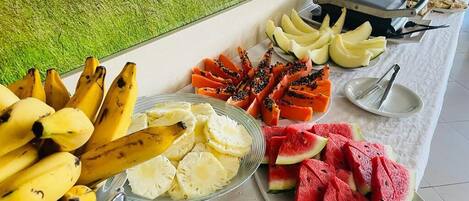 Une table de buffet proposant une variété de fruits, notamment des bananes, des ananas, des papayes et des pastèques.