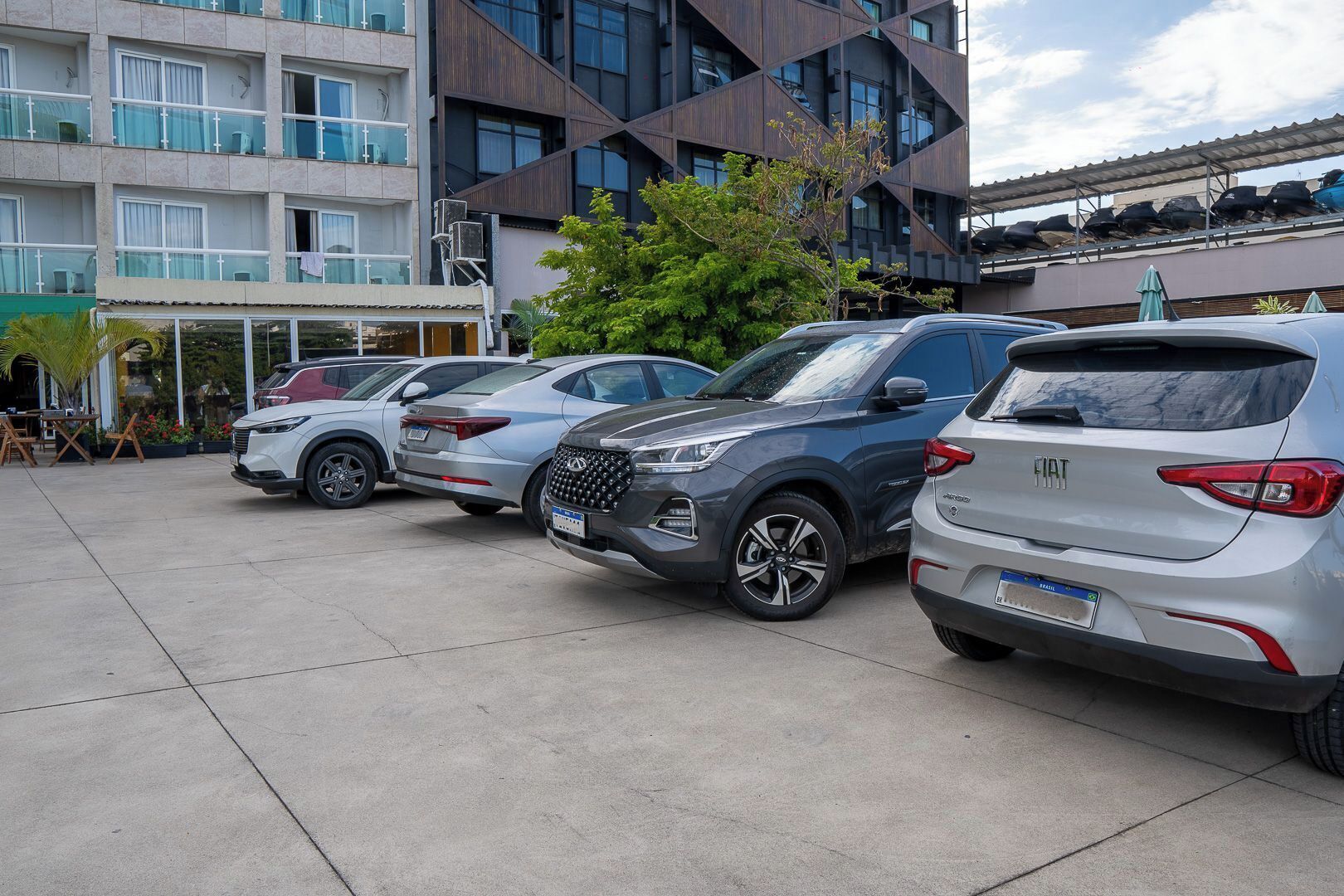 A parking area with four SUVs, a building with balconies, and a tree.