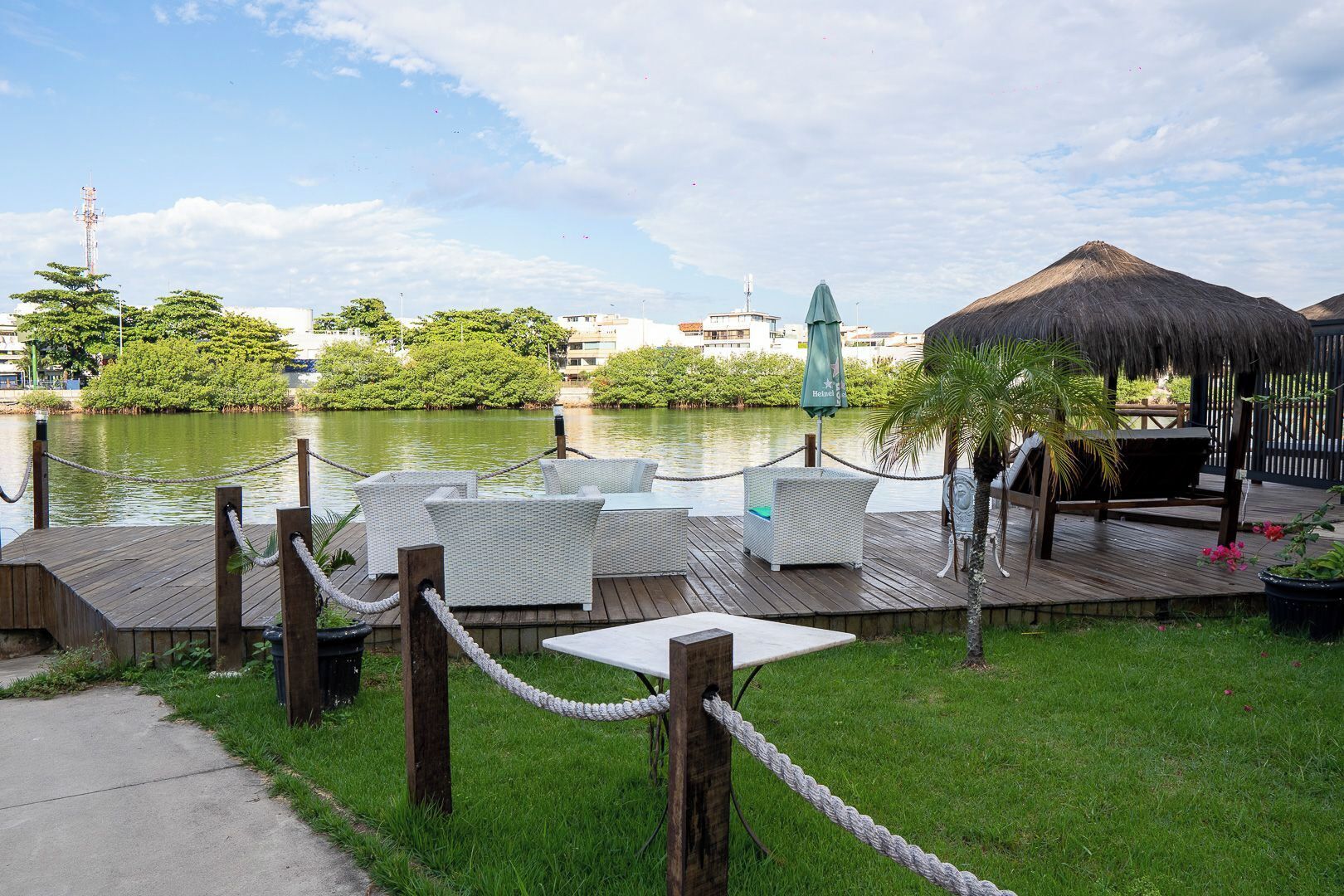 A waterfront deck with wicker furniture, a thatched-roof structure, and a view of the water and cityscape.