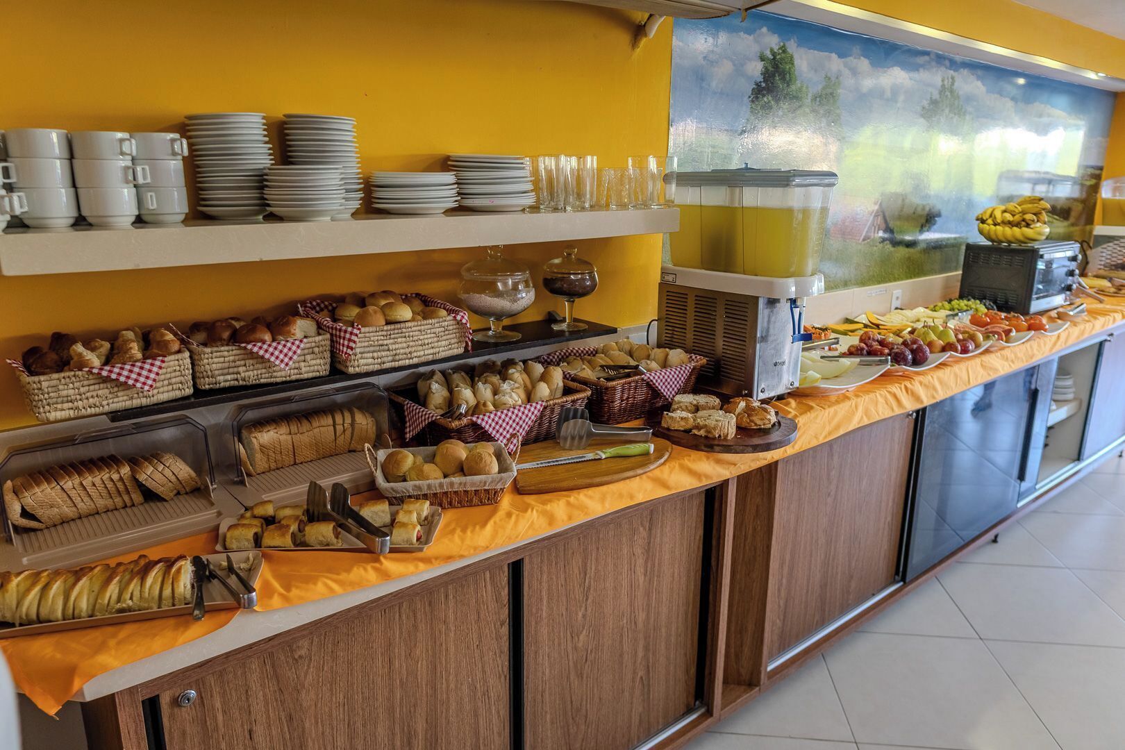 A buffet with various food items and utensils, including bread, pastries, and fruits.