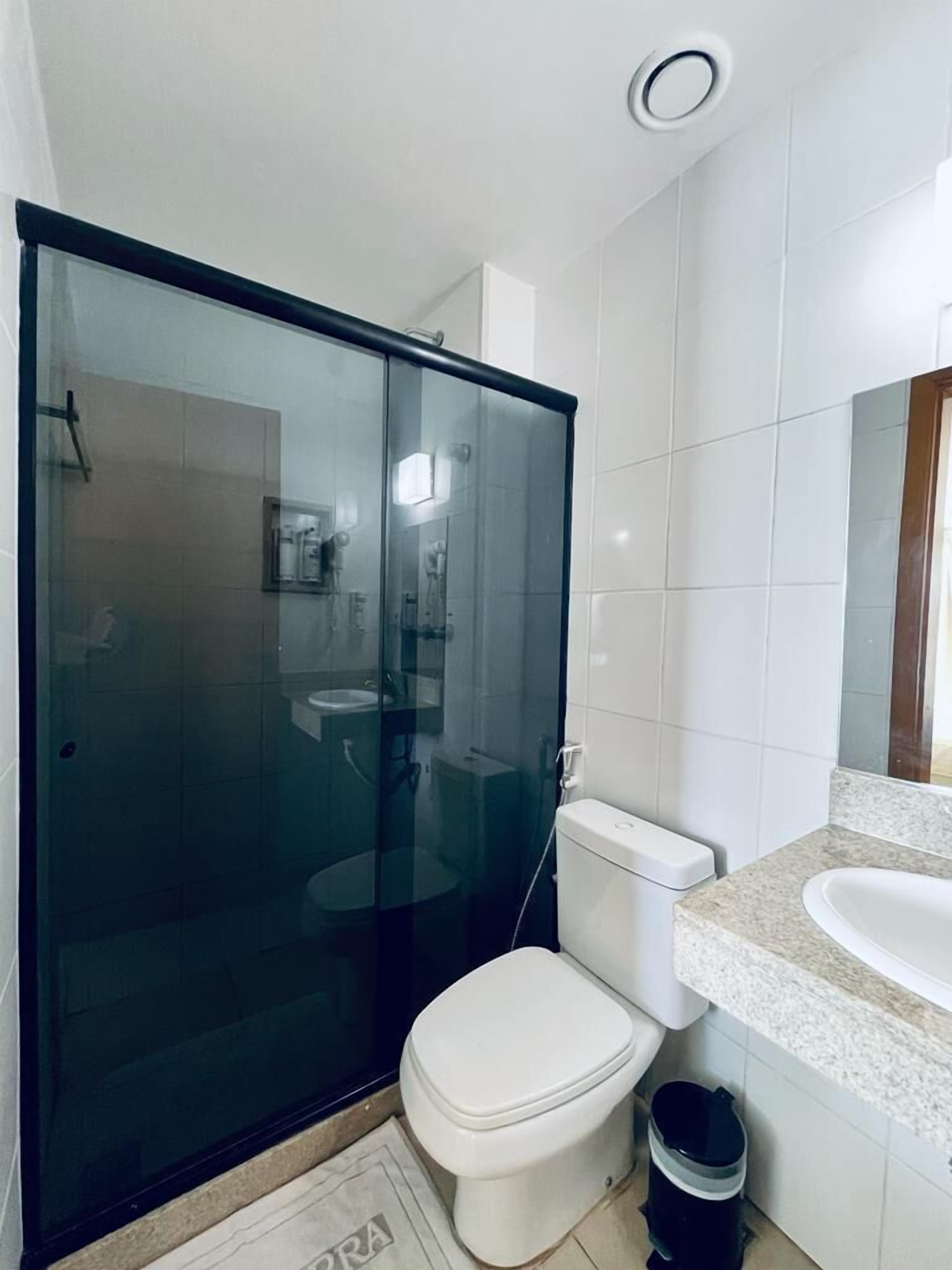 Un baño moderno con ducha envuelta en vidrio, inodoro blanco y lavamanos sobre encimera de granito.