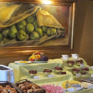 A buffet setup with various food items and a painting of fruits on the wall. - Solar De La Plaza (Salta)