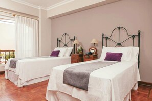 A hotel room with two single beds, a wooden nightstand with lamps, and a view of the outdoors through a window with curtains. - Solar De La Plaza (Salta)
