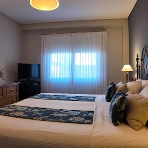 A hotel room with a bed, a television, a window with curtains, and a lamp. - Solar De La Plaza (Salta)